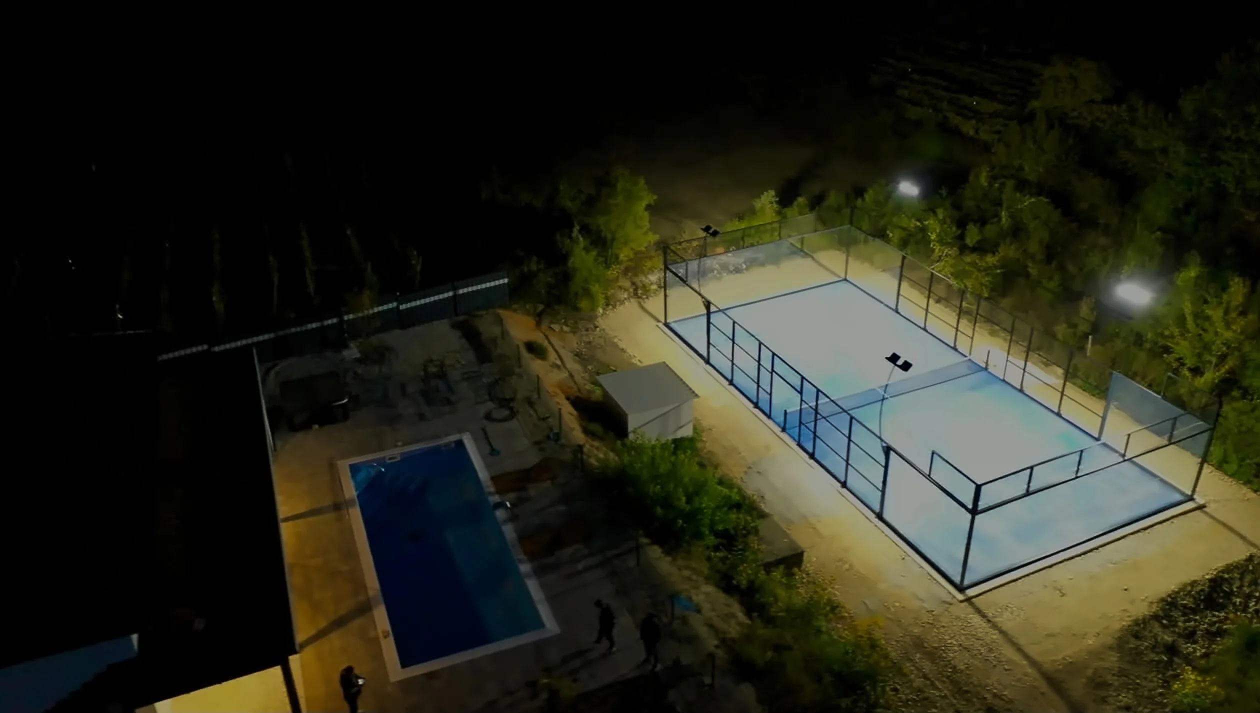 Osvijetljeni padel teren i bazen u večernjim satima, snimljeno iz zraka